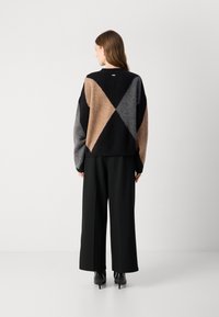 Suéter oversized em preto, castanho e cinza com padrão em diamante; textura suave e corte descontraído; combinado com calças largas pretas e saltos altos.