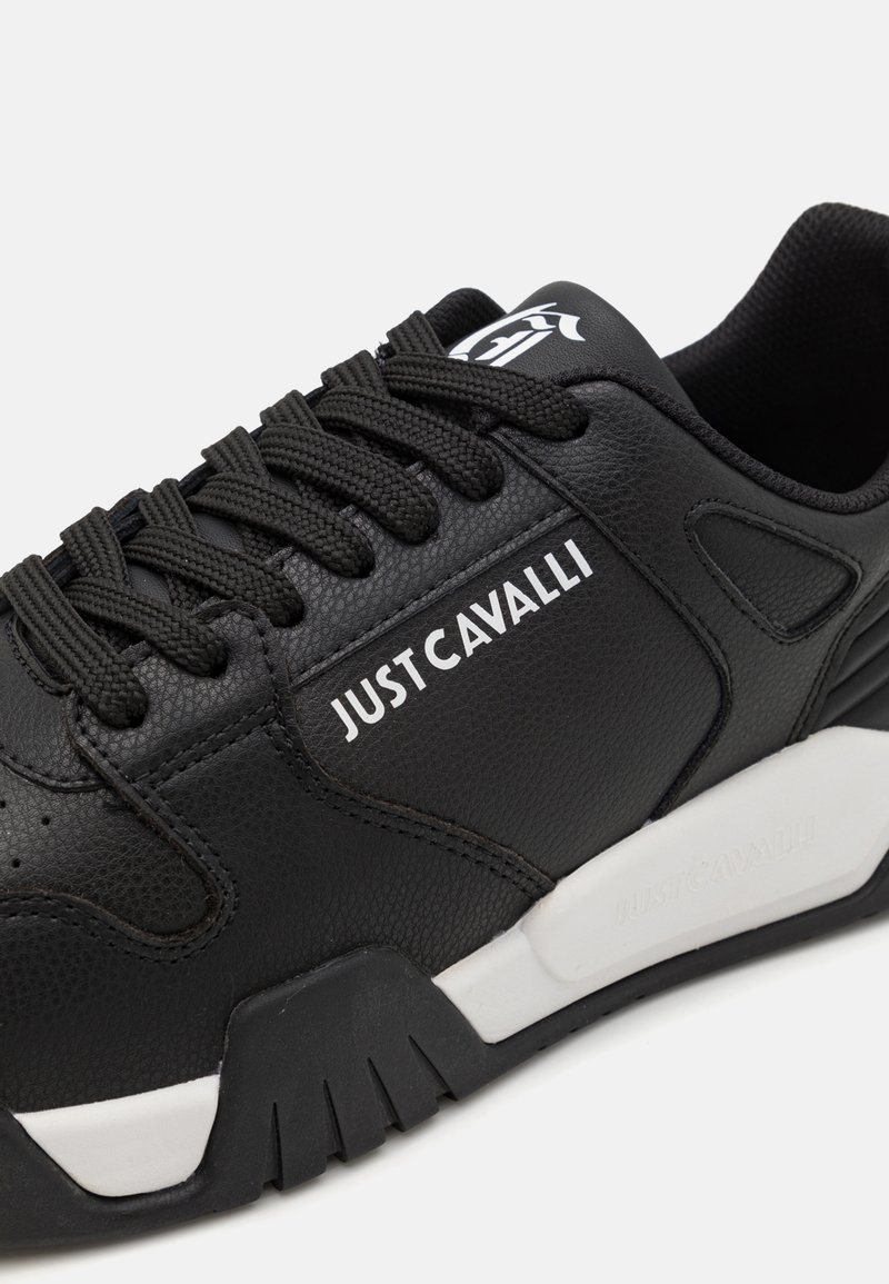 Czarne sneakersy z teksturowaną syntetyczną cholewką, z czarnymi sznurowadłami, białym logo i kontrastującą białą podeszwą. Podkreślone szczegóły wzornictwa.