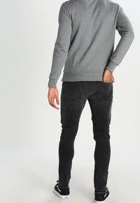 Sudadera gris con puños y dobladillo acanalados, combinada con jeans negros de corte slim que tienen bolsillos traseros y un ligero desvanecimiento, llevada con zapatillas negras.