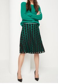 Un suéter verde acanalado combinado con una falda negra con grandes lunares verdes. La falda tiene un diseño fluido y es de longitud a la rodilla. Unos tacones negros completan el conjunto.