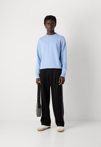 Sudadera azul clara de manga larga, pantalones anchos negros, zapatillas blancas con suelas de goma y un bolso cruzado gris.
