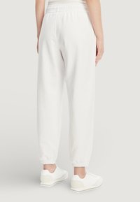 Bílé tepláky s elastickým pasem a stahovanými lemy nohavic. Vyrobené z měkkého materiálu, mají volný střih a nemají žádné viditelné vzory.