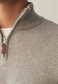 Grauer Strickpullover mit hohem Kragen und Reißverschluss. Verfügt über eine gerippte Textur und ein kleines Lederakzent in der Nähe des Reißverschlusses.