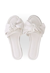 White flat sandals with a knotted fabric detail on the front. Smooth texture, open toe design, and minimalistic style. Thin sole.