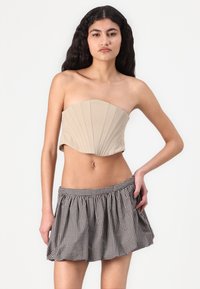 Bež ženski bandeau top z navpičnimi naborki, v kombinaciji s črno-belim karirastim flared mini krilom. Gladka tekstura, strukturiran dizajn.