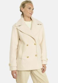 Dwurzędowy płaszcz peacoat w bladoróżowym kolorze, wykonany z miękkiej tkaniny. Posiada złote guziki, duży kołnierz oraz boczne kieszenie. Stylizowany na kremową bluzkę.