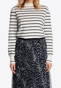 Krämsvett med marinblå ränder, rund halsringning och långa ärmar, parat med en svart kjol med en texturerad zebramönster.