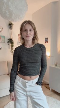 Fekete-fehér csíkozású, hosszú ujjú, rövid fazonú felső, magas derékú fehér farmernadrággal párosítva, kerek nyakkivágással és sima szövettextúrával.