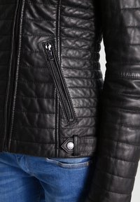 Černá kožená bunda s prošívanou texturou, vybavená bočním zipem a akcentem loga. Hladký, přiléhavý design, odolný materiál.