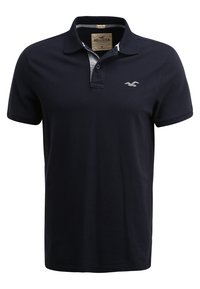 Námořnická modrá polo košile vyrobená z pružné bavlny. Obsahuje šedý límeček, zapínání na dva knoflíky a malé vyšívané logo na hrudi.