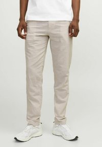 Pantalones de algodón beige con un diseño ajustado y piernas rectas, combinados con zapatillas deportivas blancas con acentos y cordones negros.