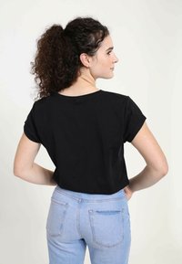 Camiseta negra de manga corta con cuello redondo, combinada con jeans de tiro alto azul claro que tienen dos bolsillos traseros.