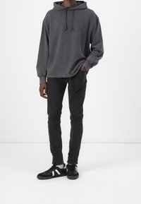 Felpa grigia scura con cappuccio e lacci, vestibilità comoda e polsini a costine, abbinata a pantaloni neri aderenti e sneaker nere con dettagli bianchi.