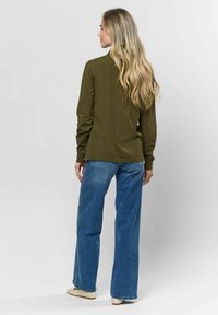 Olíva zöld, hosszú ujjú ing, egyenes szegéllyel, magas derekú kék farmernadrággal viselve. Az ing illeszkedő ujjaival és klasszikus dizájnjával rendelkezik.