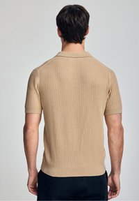 Beige lehký polo triko s krátkým rukávem a jemnou texturou. Má klasický límeček a přiléhavý lem pro štíhlý vzhled.