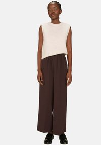 Top en maille sans manches beige clair associé à un pantalon large, loose, marron foncé. La tenue présente une texture douce et une coupe décontractée. Chaussures noires.