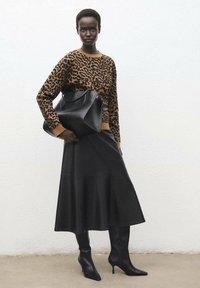 Jersey con estampado de leopardo en marrón y negro, combinado con una falda de cuero negra. Botas de punta negra y un bolso de mano estructurado negro completan el conjunto.
