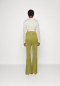 Pantalon vert olive clair, texture côtelée, coupe évasée, associé à un chemisier crème à manches longues plissé. Pas de motifs ni de logos visibles.