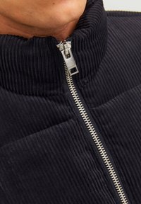Czarna kurtka ze sztruksu z wysokim kołnierzem i zamkiem błyskawicznym z przodu, z pionową prążkowaną fakturą oraz kontrastującym, srebrnym uchwytem zamka.