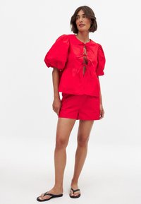 Haut rouge à manches bouffantes avec un décolleté en trou de clé, associé à un short rouge assorti. Le tissu semble lisse, avec une coupe décontractée et un design casual.