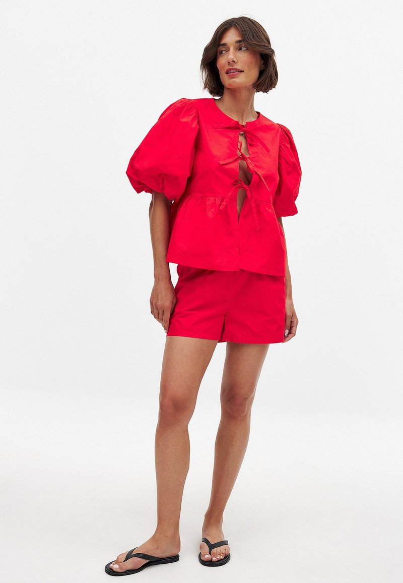 Haut rouge à manches bouffantes avec un décolleté en trou de clé, associé à un short rouge assorti. Le tissu semble lisse, avec une coupe décontractée et un design casual.