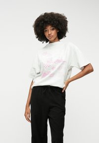 Valge ülepaisutatud t-särk roosa graafilise kujundusega; ümar kaelus, lühikesed varrukad. Mustad, lõdvad püksid paelaga vööl, ribakujundusega.