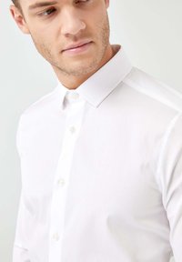 Weißes Hemd mit Button-Down-Kragen, glatter Textur und langen Ärmeln. Verfügt über eine sichtbare Knopfleiste und ein zurückhaltendes Design.