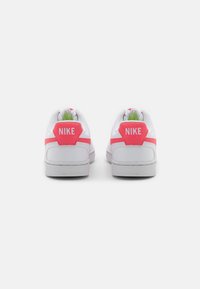 White Nike sneakers with pink accents, featuring a textured outsole, hexagonal heel patch, and a lace-up design.