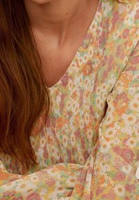 Bluse mit Blumenmuster, die über einen V-Ausschnitt, lange Ärmel und einen leichten, strukturierten Stoff in sanften Farben von Gelb, Rosa und Grün verfügt.