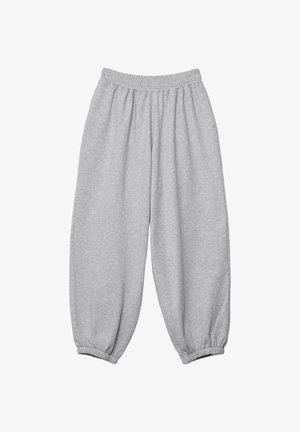Personne portant un pantalon de survêtement ample gris clair et une chemise blanche boutonnée relevée pour montrer le ventre et la zone de la taille.