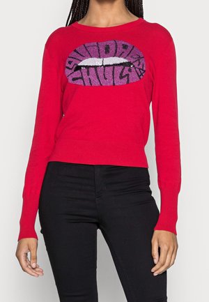 Red long-sleeve sweater with glittery purple lips graphic and black text, worn with black pants, showing torso and arms of person.