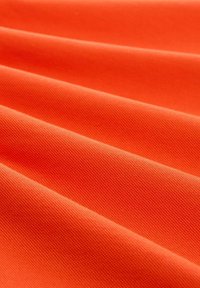 Textúrovaná látka v žiarivej oranžovej farbe, ktorá predvádza diagonálne záhyby a hladký povrch. Materiál vyzerá trvanlivo s jemným vzorom tkaniny.