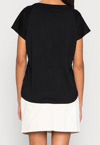 Camiseta de algodón negra de manga corta y con bajo redondeado, combinada con una falda clara de longitud a la rodilla. Se ve la vista desde atrás.