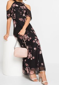 Svart blommig klänning med avklippta axlar, prydd med rosa rosor, flödande tyg och en volangkrage. Kombinerad med en ljusrosa handväska.