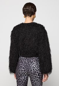 Maglione corto nero peloso con maniche lunghe, con finitura testurizzata e orlo a coste; indossato sopra leggings grigi con stampa leopardata.