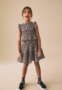 Šaty se vzorem leopardí kůže s volánkovými rukávy, vícepatrovou sukní, tmavě béžová látka. Černé tenisky s bílými pruhy, hnědé ponožky. Neutrální pozadí.