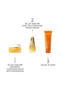 Trois produits de soin Darphin : un baume nettoyant jaune dans un petit pot, un sérum doré dans un flacon en verre, et un tube d'écran solaire orange.