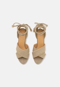 Sandales à plateforme tissées beiges avec des brides croisées, en matériau texturé, lanières de cheville et semelle intérieure lisse. Caractéristiques d'un design à bout ouvert et plat.