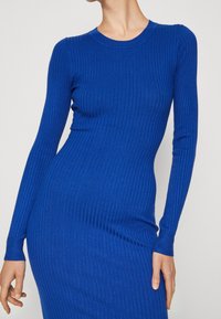 Geripptes, langärmliges Kleid in tiefem Blau. Es verfügt über eine figurbetonte Silhouette und einen runden Halsausschnitt. Das Material ist weich mit einer glatten Textur.