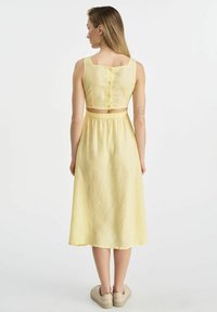 Żółta lniana sukienka dwuczęściowa z krótkim topem o kwadratowym dekolcie i zapięciem na guziki z tyłu, oraz zwiewną, długości do kolan spódnicą.
