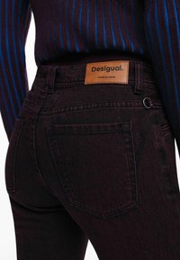 Tumedad purple teksad, millel on struktureeritud viimistlus, millel on tan nahast silt "Desigual" vööl ja tagatasku detailidel.