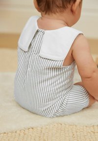 Jumpsuit a rayas en tejido gris y blanco, que presenta un cuello contrastante, cierre trasero con botón y una textura suave, con un corte relajado.
