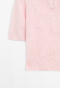 Světle růžový svetr s krátkým rukávem vyrobený z měkkého pleteného materiálu. Obsahuje kulatý výstřih a malou knoflíkovou dekoraci blízko límce.