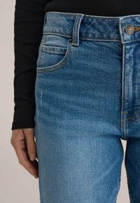 Svetlomodré riflové nohavice s vysokým pásom, s prešívanými vreckami, oranžovými švami a klasickým zapínaním na gombík.