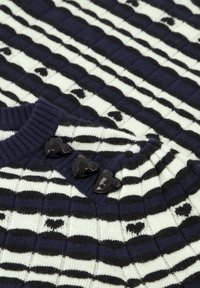 Pletený svetr s námořnickým a krémovým vzorem, texturovanými pruhy a třemi černými knoflíky ve tvaru srdce na výstřihu.