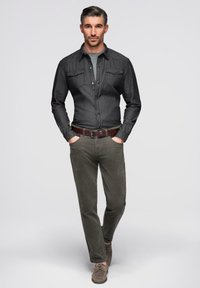 Chemise en denim foncé à boutons avec poches poitrine, associée à un pantalon en velours côtelé vert olive coupe slim et des chaussures marron, sur un fond uni.