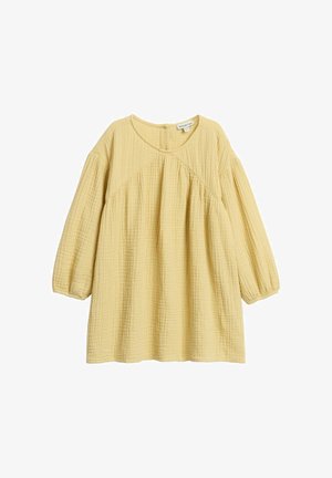 Väljä istuva mallinen, pitkähihainen vauvan keltainen paita, jossa pyöreä pääntie, kerätty kangaspinta ja vino sauma rinnan yli.