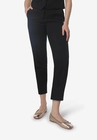 Pantalones negros ajustados con un corte recto, con bolsillos laterales y una textura suave. Combinados con bailarinas doradas claras con un detalle de lazo.