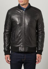 Zwarte leren bomberjack met ritssluiting, geribde manchetten en een gladde textuur. Voorzien van zijzakken en een ritszak op de mouw.