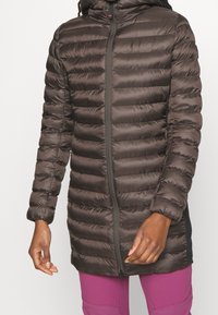 Mörkbrun vadderad jacka med dragkedja framtill, med quiltade sektioner, hög krage och smal passform. Detaljer inkluderar sidopaneler och elastiska muddar.